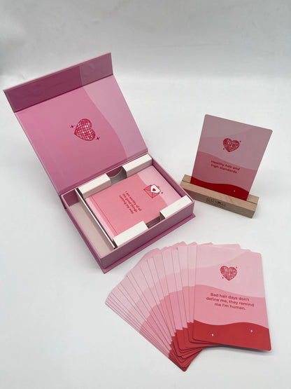 Self Love Hair Club affirmation deck with open pink box, wooden display stand, and fan of pink affirmation cards featuring self-love affirmations.  
