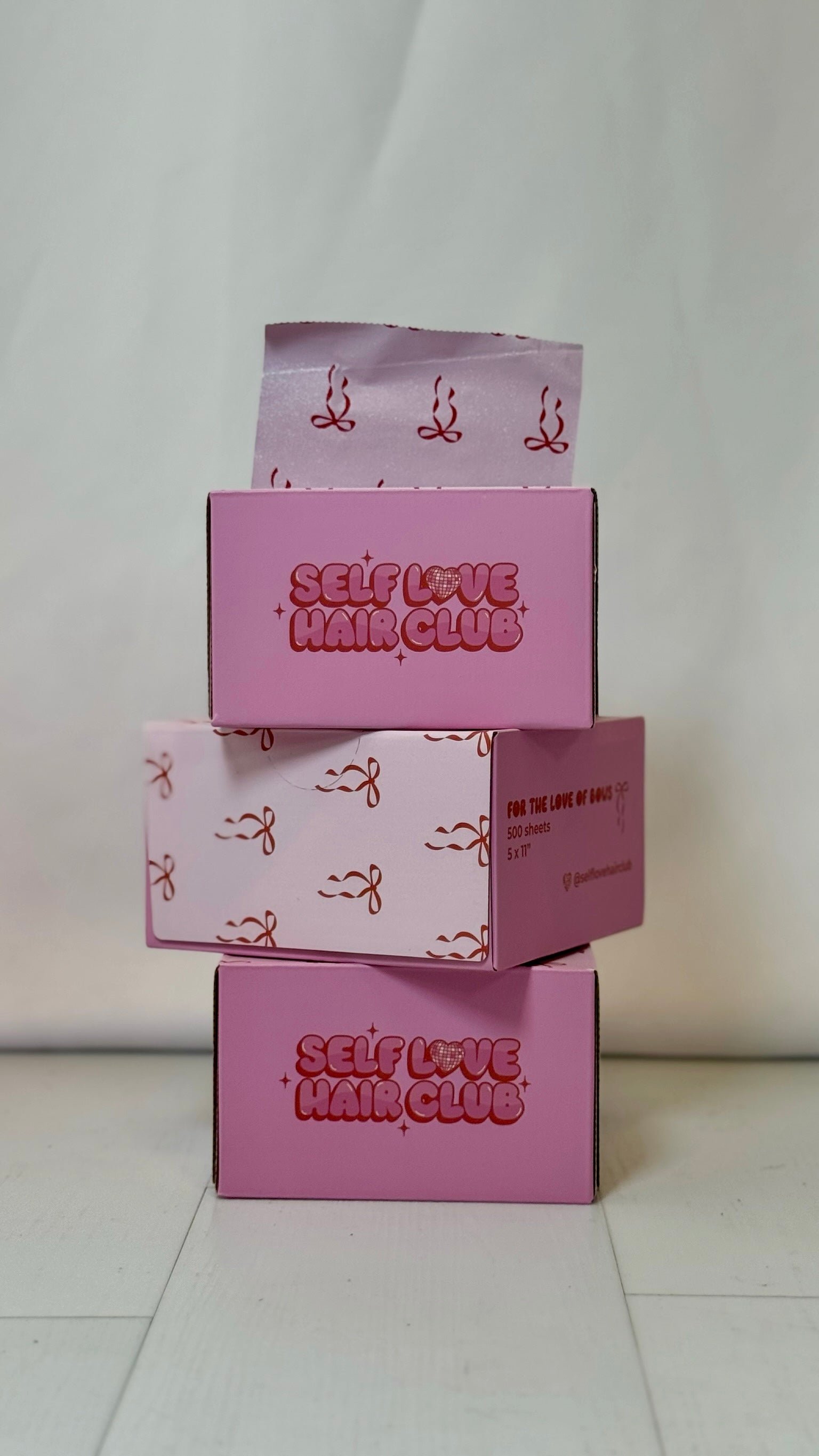 Stack of pink Self Love Hair Club foil boxes on a white background